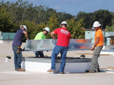 Four Buffington Brothers commercial HVAC technicians in hard hats setting curb on a flat commercial rooftop.