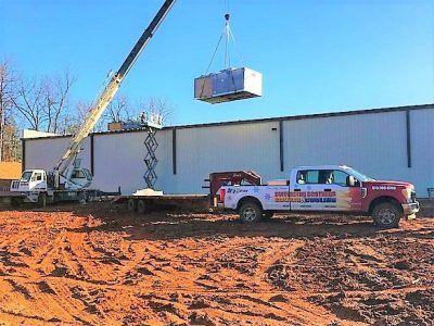 Crane lifting a large commercial HVAC unit with Buffington Brothers truck on site.