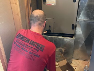 Buffington Brothers technician in a red company shirt working on a residential furnace cabinet.