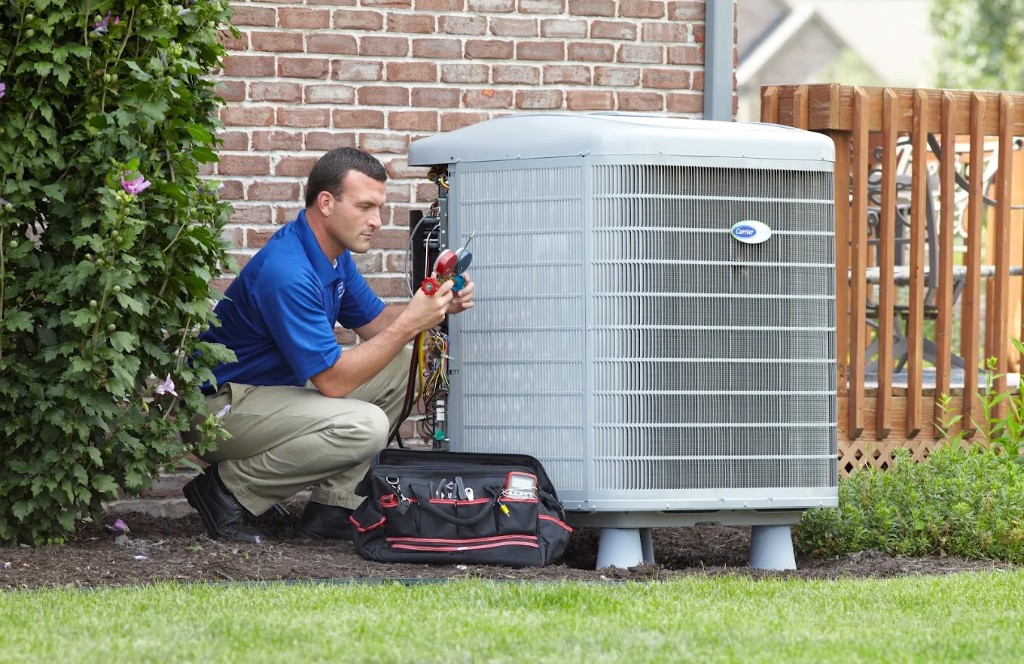 Technician checking refrigerant pressures on a Carrier outdoor air conditioning unit with professional tools.